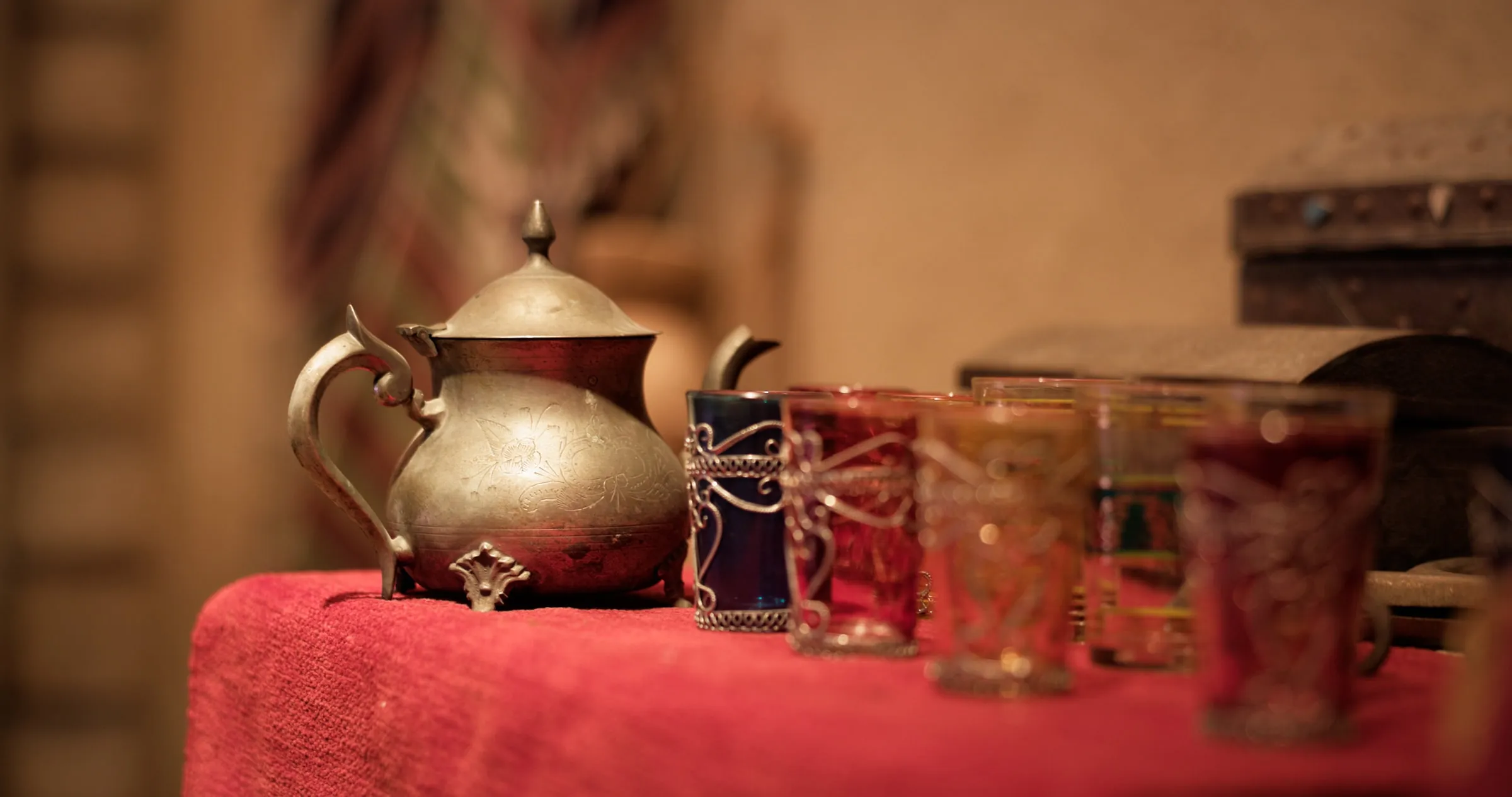 An engraved dallah beside decorated tea glasses on a red cloth