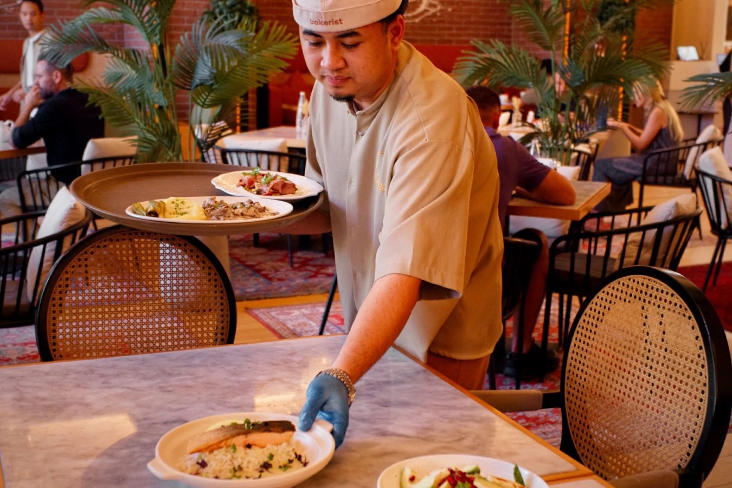 A chef plating a dish at a marble pass in a busy restaurant dining room