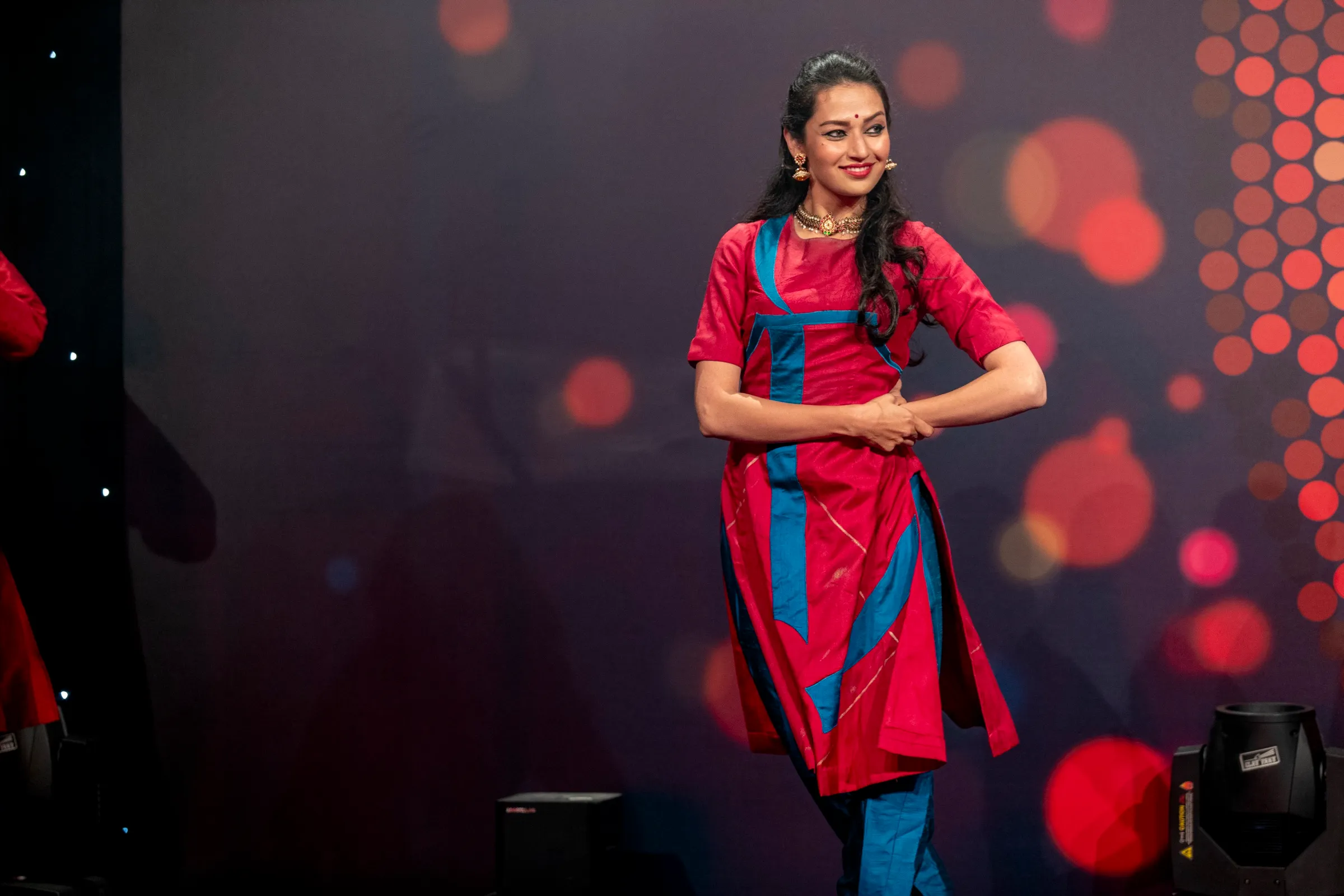 A classical dancer in a red and blue costume performing under warm bokeh lighting
