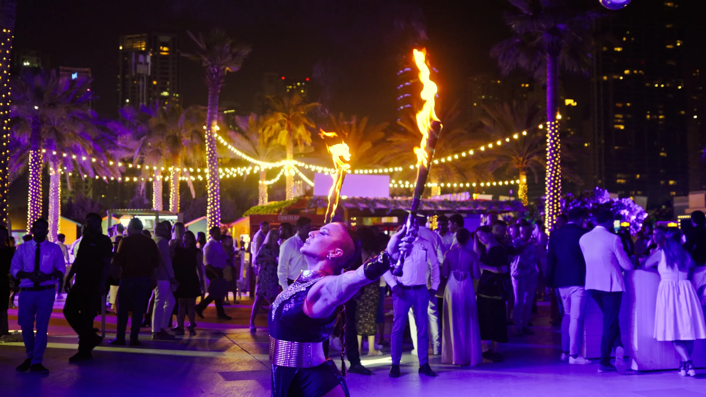 A fire performer raising a lit torch above a crowd at an outdoor evening gala
