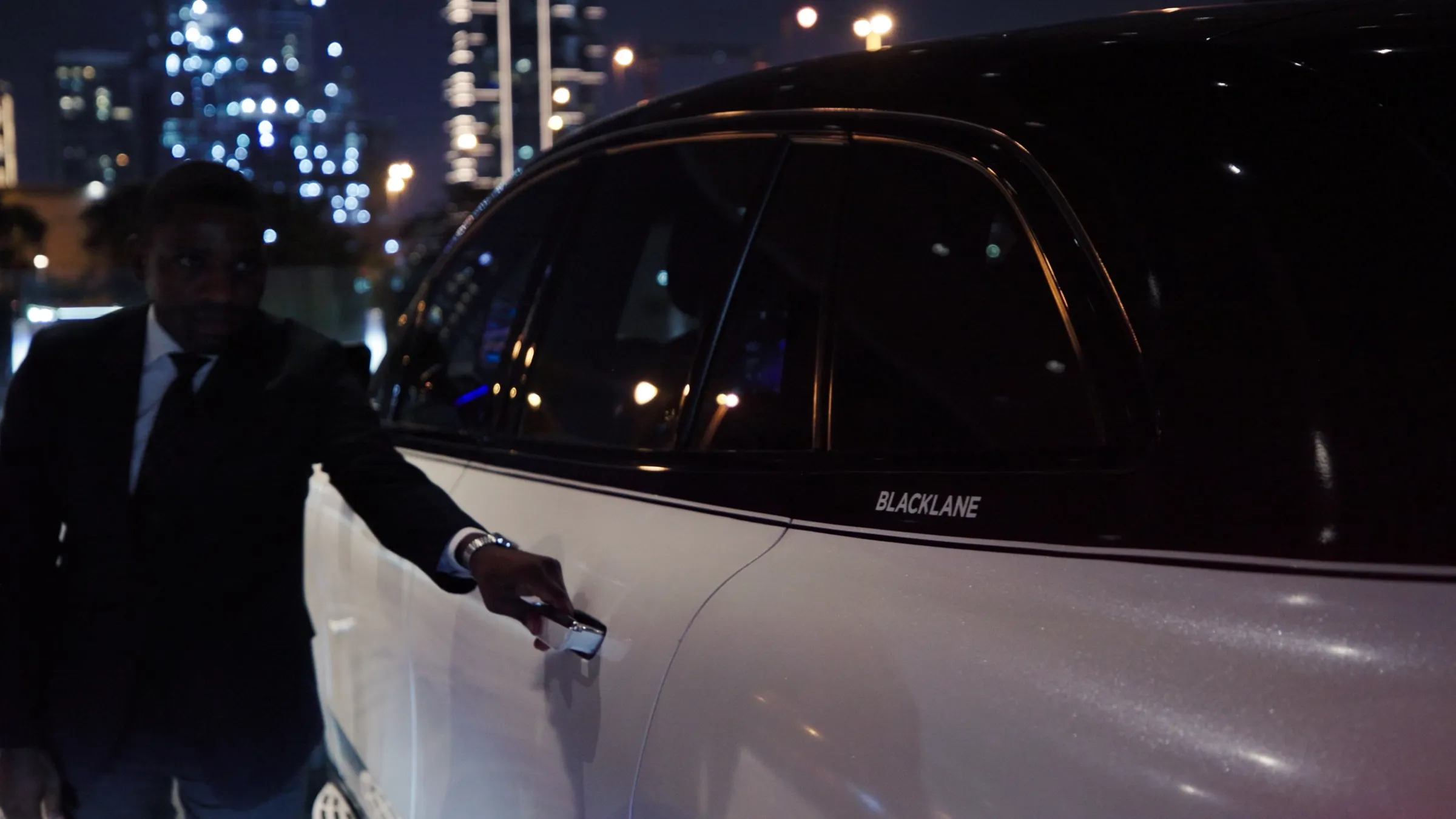 A luxury car photographed at night with a figure beside the open door