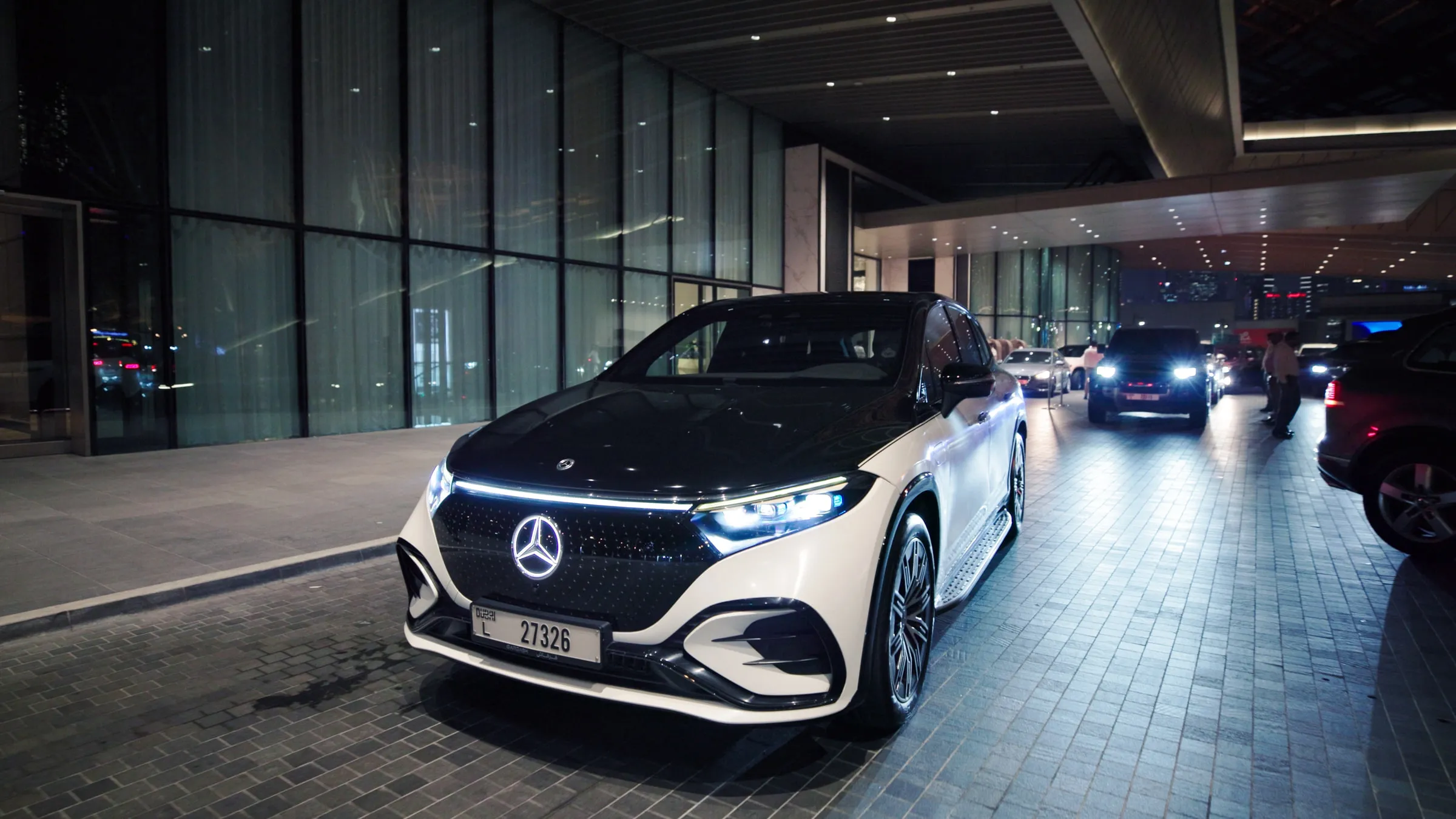 A white electric saloon at the head of an arrival line outside a lit venue at night